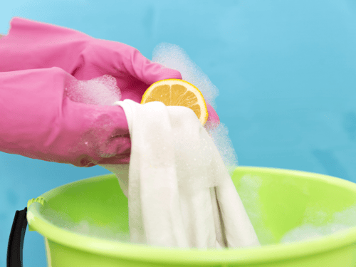 mujer con guantes plásticos limpiando un paño de cocina con un limón en una cubeta verde