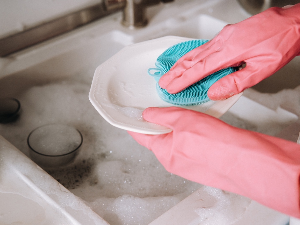 manos con guantes rosados lavando un plato pequeño en el lavaplatos