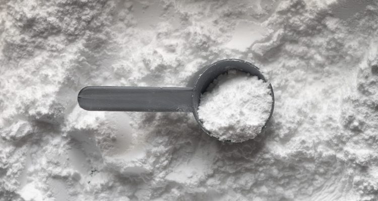 una cuchara medidora con harina y gorgojo sobre un fondo de harina esparcida