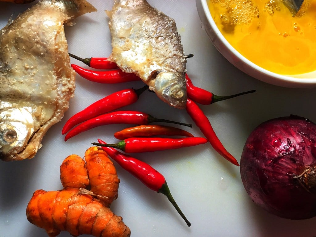 alimentos esparcidos sobre una mesa, unos sobre otros: hay pescado, pimientos, zanahorias y cebolla
