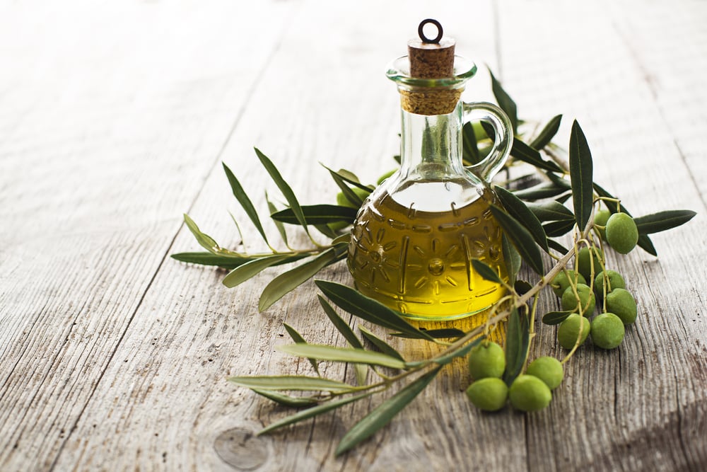 Fasco de vidrio con aceite de oliva rodeado de hojas y frutos de olivos