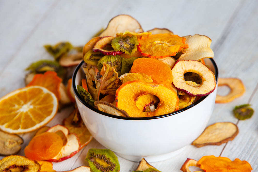 pocillo blanco con alimentos deshidratados como naranjas, kiwi y manzanas en rodajas