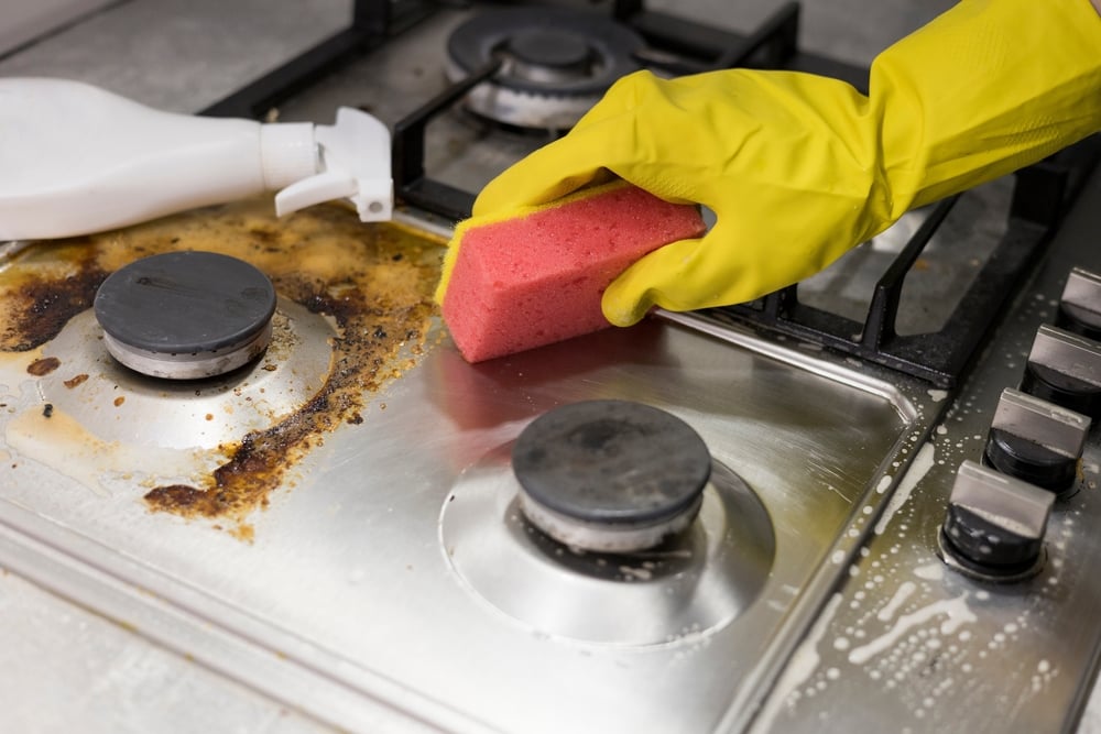 una mano con una esponja que muestra cómo limpiar la grasa de la cocina